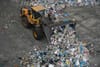 A yellow truck pushes a mound of recylables.