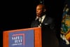 NYC Mayor Eric Adams in a black suit speaking behind a podium with a sign that says "Safe and Just Communities."