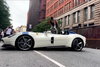 A skateboarder jumping over a white sports car on a Manhattan street.