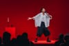 Jes Tom in oversized chic clothing with their arms outstretched, while performing "Less Lonely"